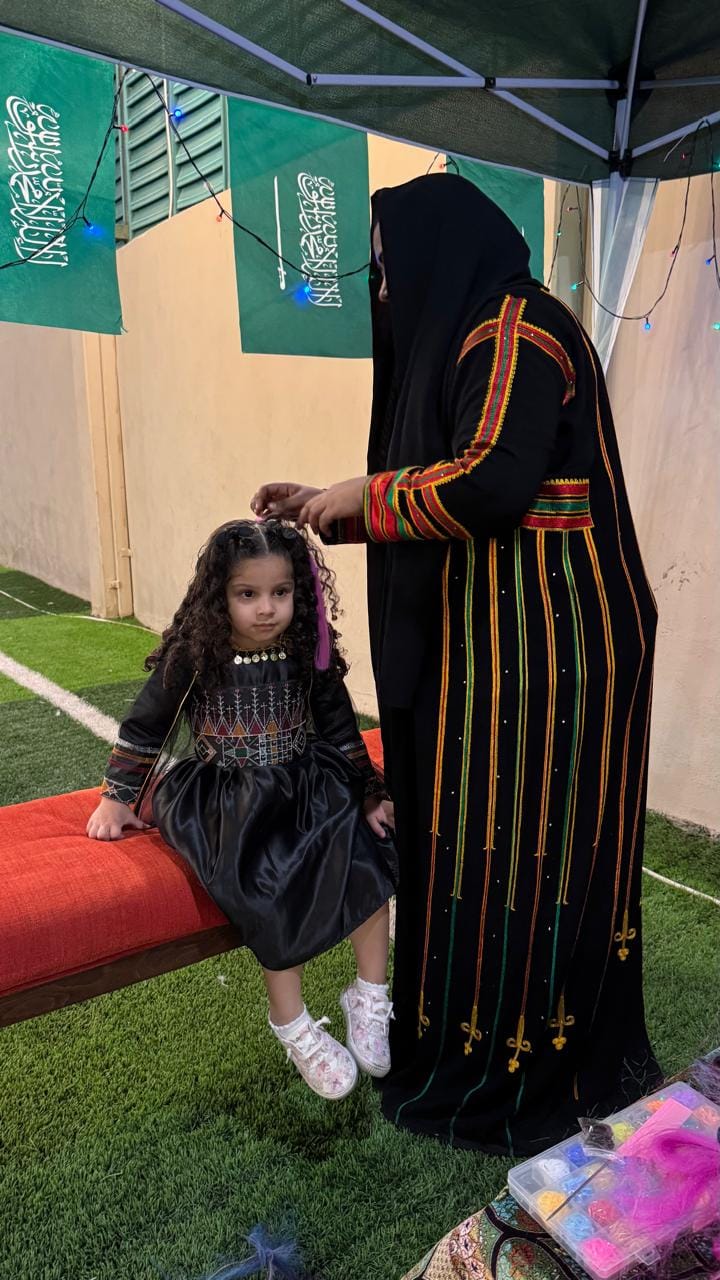 Henna artist in traditional embroidered abaya with young guest