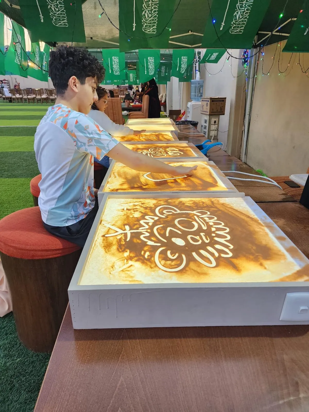 Child doing sand art on lit tables under green flags