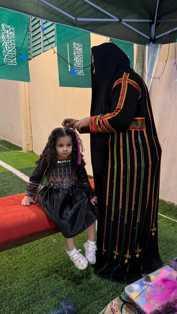 Girl in traditional dress having hair styled by woman in heritage costume